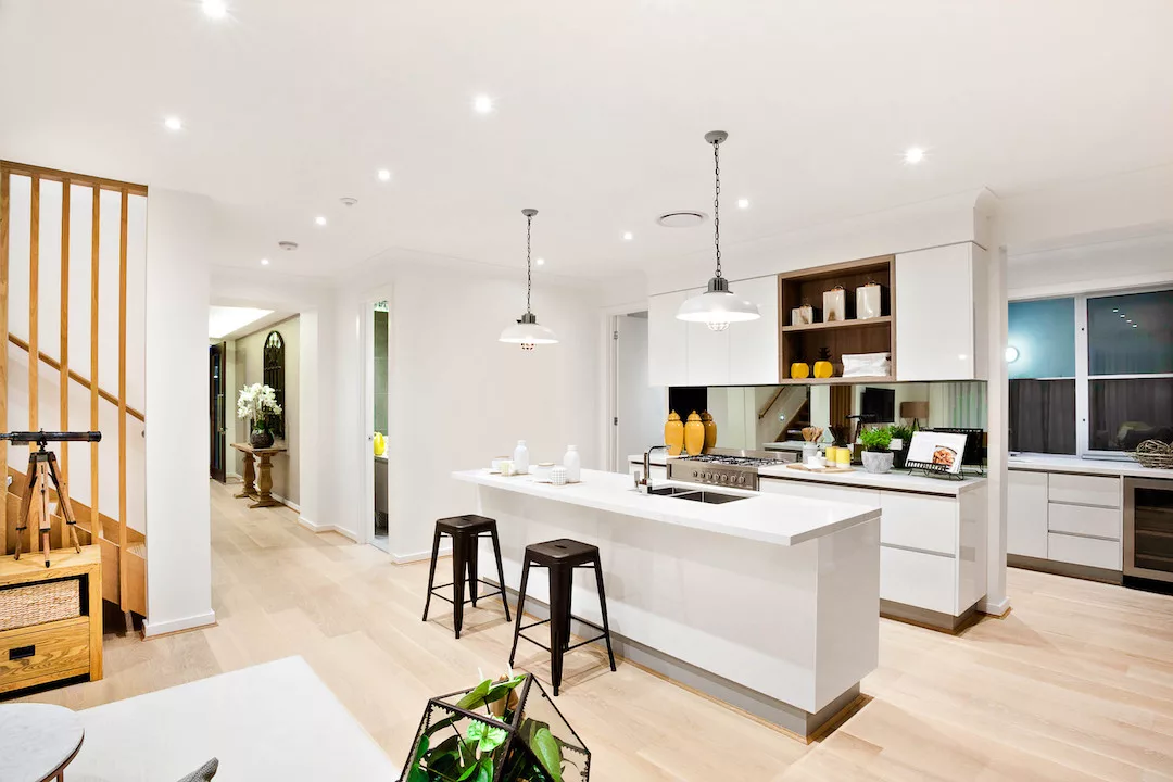 Modern kitchen with white walls illuminated by hanging lamps at night beside the wooden hallway through the luxury house and stairs