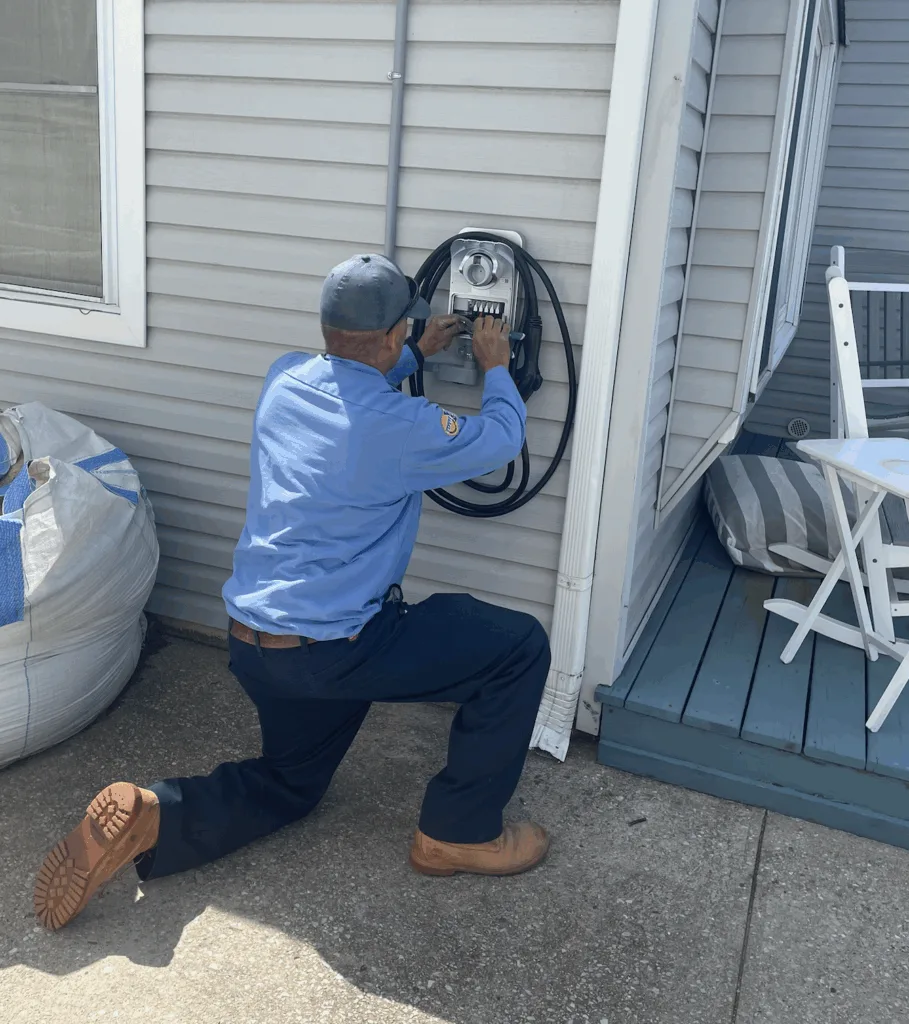 Licensed electrician installing a Level 2 EV charger on the exterior of a Nassau County home, wiring the unit with clean conduit and professional tools.