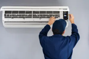 Electrician wiring a ductless mini-split air conditioner on an interior wall, performing detailed electrical work with a screwdriver.
