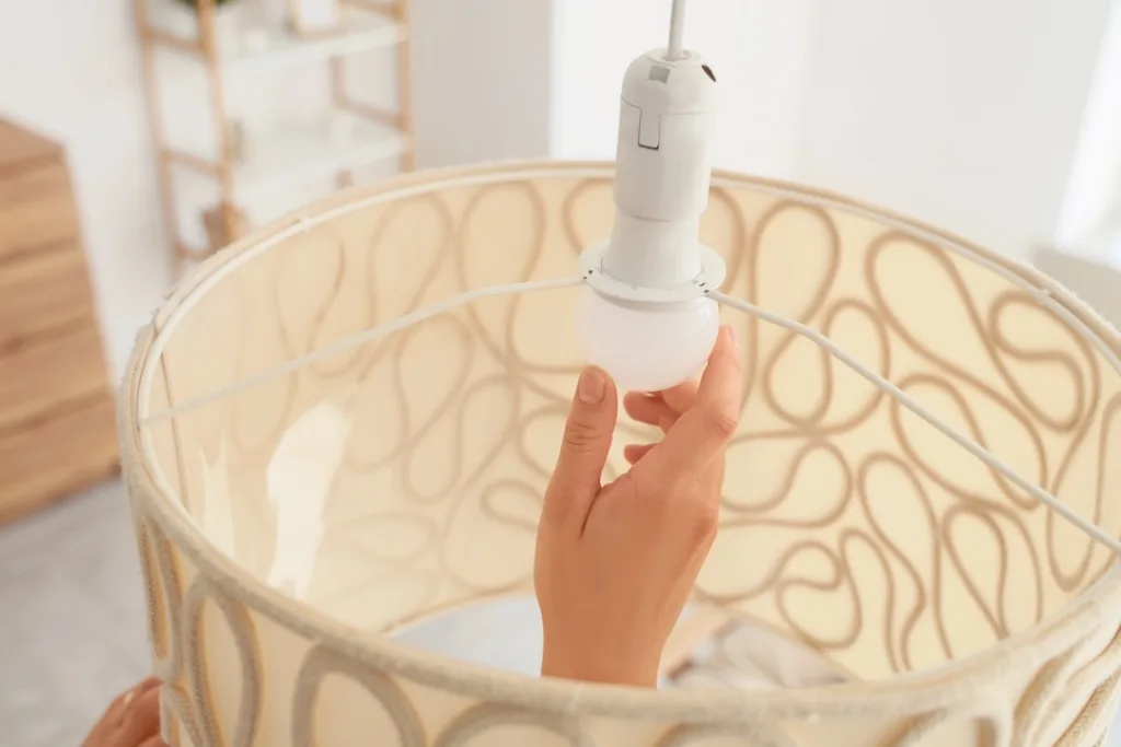 Female hand screwing light bulb into stylish lamp at home, closeup