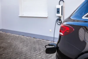 Generic electric vehicle EV hybrid car is being charged from a wallbox on a contemporary modern residential building house